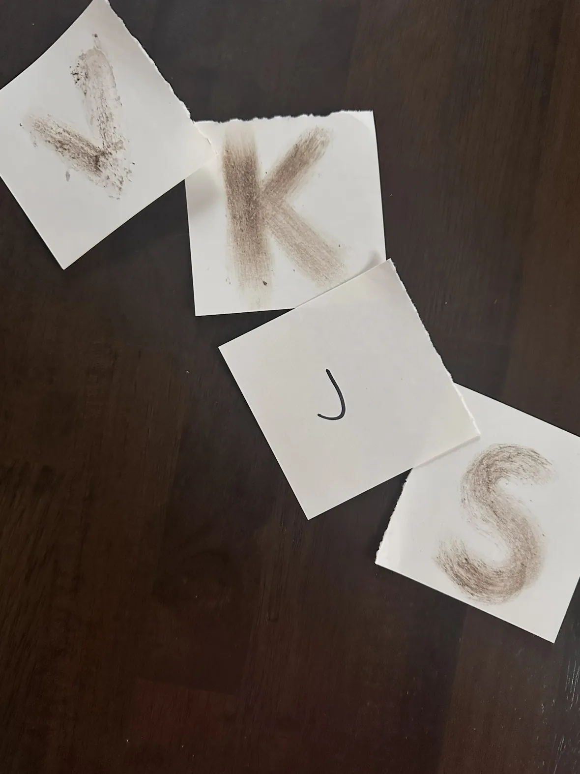 The letters V, K, J, S traced in dirt on wood — Inside Passage promo